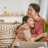 Asian girl with bunch of flowers hugging her happy mother sitting on sofa in living room, horizontal portrait